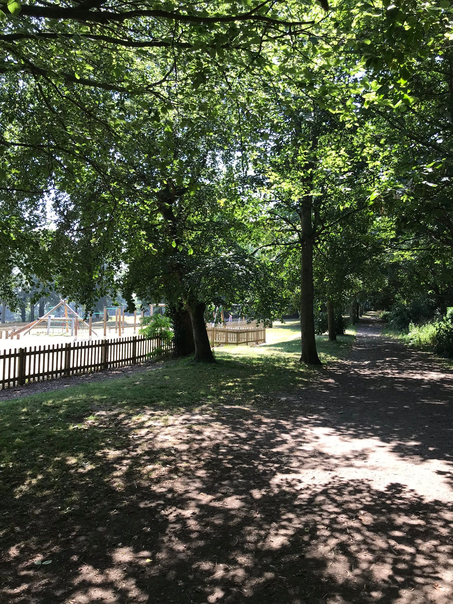 Shady walkway through the trees towards the children's play area at King George VI Memorial Park